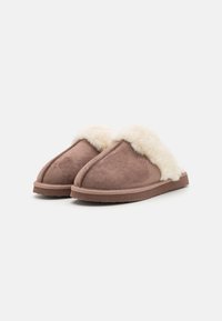 Chaussons en daim marron avec une doublure en polaire crème fluffy, un design à bout fermé et une semelle en caoutchouc texturé. Style hybride, chaussure décontractée.