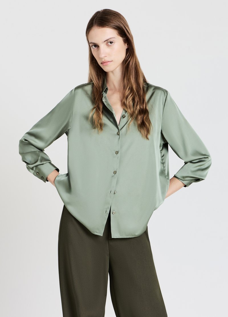 Camicia verde in satin con vestibilità rilassata, maniche lunghe, chiusura con bottoni e una texture liscia, abbinata a pantaloni verde scuro.