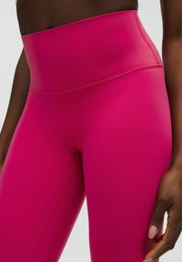 High-waisted pink leggings made of smooth, stretchy material. Features flatlock seams and a tapered design for a snug fit.