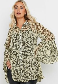 Genomskinlig, blommig blus i grönt och krämigt. Har en knappslå fram, krage och plisserade, utsvängda ärmar. Lättviktigt tyg.