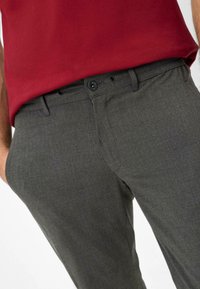 Pantalons gris sur mesure avec une finition texturée, dotés d'une fermeture à bouton, de poches latérales et d'une coupe slim. Associés à un haut rouge.