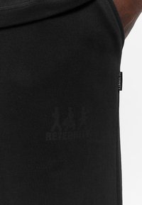 Black tank top with a smooth texture, featuring a subtle graphic print and a small tag labeled "RETERNITY" at the side seam.