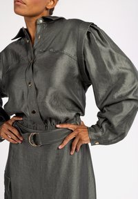 Gray denim shirt dress with a collared neckline, puffed sleeves, elastic waist, and a belt featuring a circular gold buckle.