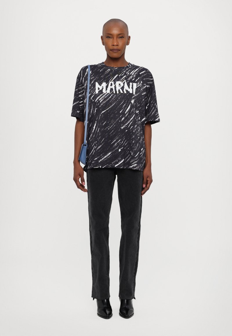 Oversized T-shirt i sort-hvidt mønster med "MARNI" tekst, parret med sorte jeans og sorte hælede støvler. En blå skuldertaske er inkluderet.
