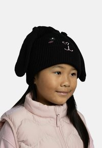 Black knitted beanie featuring bunny ears, embroidered facial features in beige and pink, ribbed texture, worn over a light pink puffer vest.