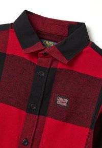 Camicia a quadri rossa e nera per bambini con bottoni neri, colletto e un'etichetta "EDIZIONE LIMITATA" sulla tasca del petto.