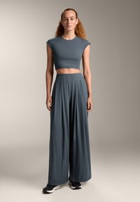 Szürke crop top rövid ujjakkal, laza, magas derekú, széles lábú nadrággal párosítva. Simább textúra, könnyű anyag, és lezser szabás.