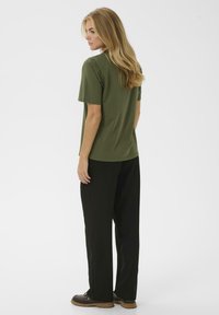 T-shirt vert olive à manches courtes avec une coupe décontractée, associé à un pantalon noir ample et des chaussures marron foncé, vu de dos.