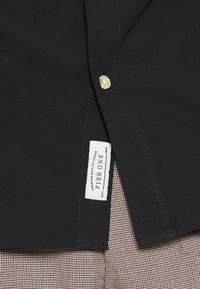 Czarna koszula z guzikiem i metką z napisem "PIERONE". Tkanina o fakturze z kontrastującym, paskowanym wzorem pod spodem.