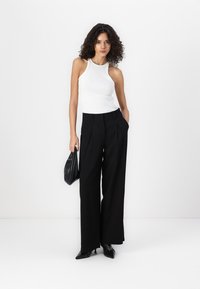 White sleeveless top, high neck, paired with black wide-leg trousers featuring pleats, and black pointed-toe heels. Black handbag in hand.