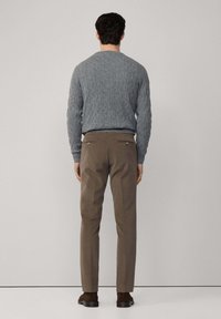 Szary sweter w warkocze z okrągłym dekoltem, zestawiony z brązowymi spodniami z tylnymi kieszeniami i subtelnymi detalami przeszyć.