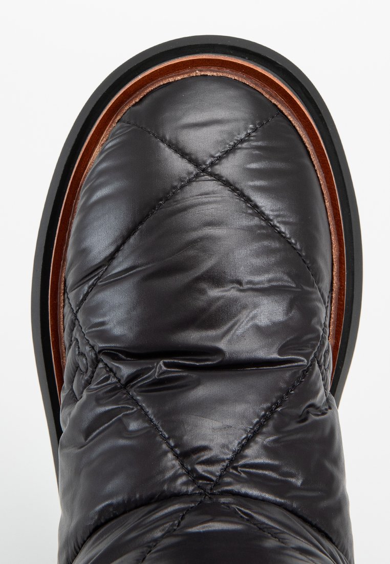 Parte superior de bota acolchada negra con una textura suave y brillante y ribete de cuero marrón. Suela exterior de goma negra con un diseño para mayor tracción.
