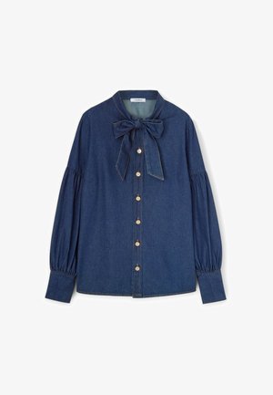 Camicia di jeans di colore blu scuro, con colletto a fiocco, maniche lunghe a sbuffo e sette bottoni in ottone lungo la parte anteriore. Texture liscia.