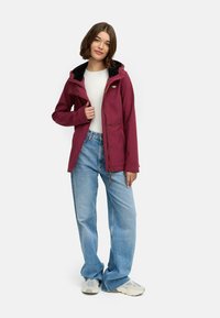 Burgundy huppari takki mustalla fleece-vuorella, jossa on vetoketjukiinnitys, etutaskut ja rento leikkaus, päällä valkoinen paita ja farkut.