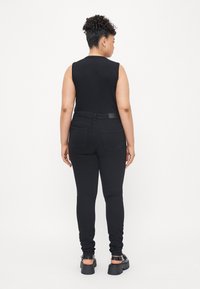 Black sleeveless top paired with skinny black jeans, featuring a high waist and back pockets, with chunky black sandals.