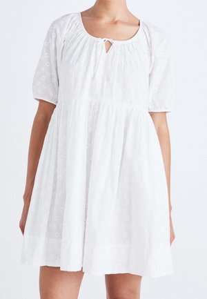 Vestido de algodón blanco con mangas cortas abullonadas, escote redondo y detalle de ojal. Presenta un diseño fluido y un patrón de bordado floral.