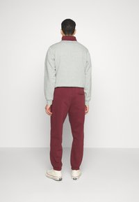 Grau Fleece-Pullover mit burgunderfarbenem Kragen, kombiniert mit kastanienbraunen Jogginghosen. Stoff aus Baumwollmischung, elastische Bündchen und Rückentaschen. 