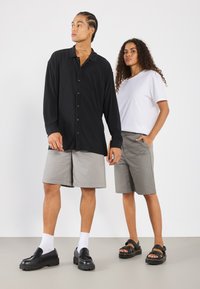 Black long-sleeve shirt with button closure, grey shorts, and black shoes. White t-shirt under the shirt, solid colors, and casual design.