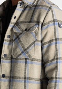 Wollen mix flanellen overhemd, beige met een blauw- en zwartgeruite patroon, met twee borstzakken en zwarte drukknoopsluitingen.