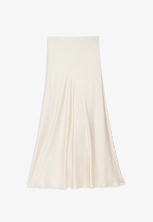 Kvinde iført en cremefarvet satin halterneck-kjole og matchende åbne pumps, stående mod en ensartet lys baggrund.