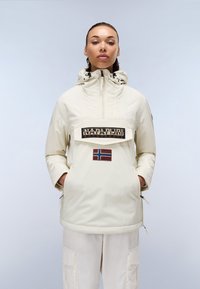 Lys beige genserjakke med hette, frontlomme og brodert logo. Har en norsk flaggplaster og sidelommer for enkel påkledning.