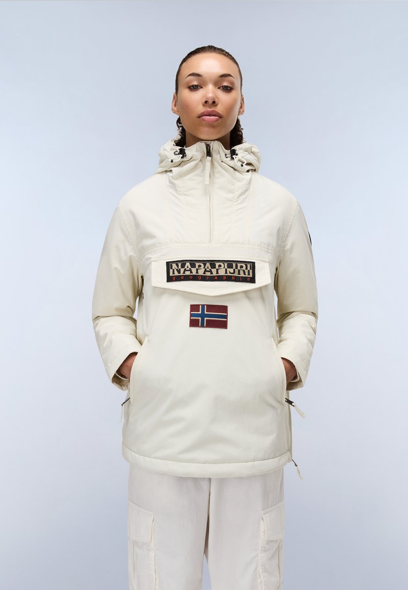 Lys beige genserjakke med hette, frontlomme og brodert logo. Har en norsk flaggplaster og sidelommer for enkel påkledning.