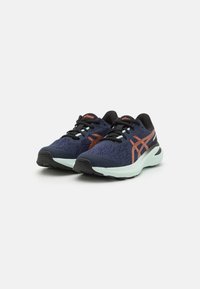 Des chaussures de sport bleu foncé présentent une tige en maille respirante, des accents orange, des lacets noirs et une semelle intermédiaire vert clair avec une semelle extérieure texturée.