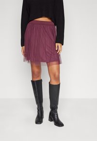 Lila tyllkjol med en samlad elastisk midja, lagerdesign, kombinerad med höga svarta läderstövlar. Kjolen har en genomskinlig textur.