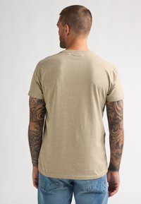T-shirt beige à manches courtes avec un col rond, en tissu doux ; présente des coutures visibles et une coupe confortable. Design décontracté.