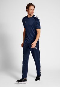 Tenue de sport bleu marine comprenant un t-shirt à manches courtes et un pantalon fuselé, fabriquée en tissu lisse, arborant un logo et des accents blancs contrastants.