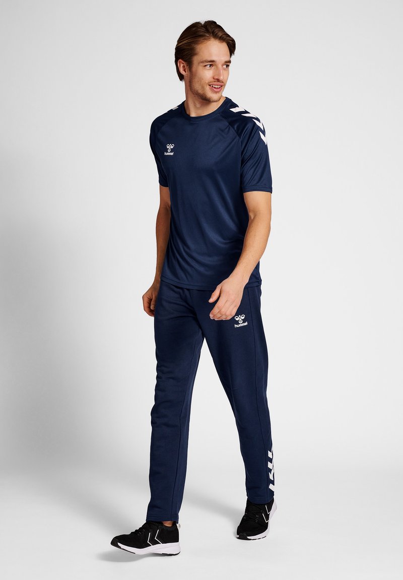 Tenue de sport bleu marine comprenant un t-shirt à manches courtes et un pantalon fuselé, fabriquée en tissu lisse, arborant un logo et des accents blancs contrastants.