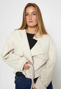 Chaqueta de gran tamaño en color crema con cuello de solapa, grandes bolsillos y cintura ceñida con cinturón. Confeccionada con una tela suave y de textura lisa.