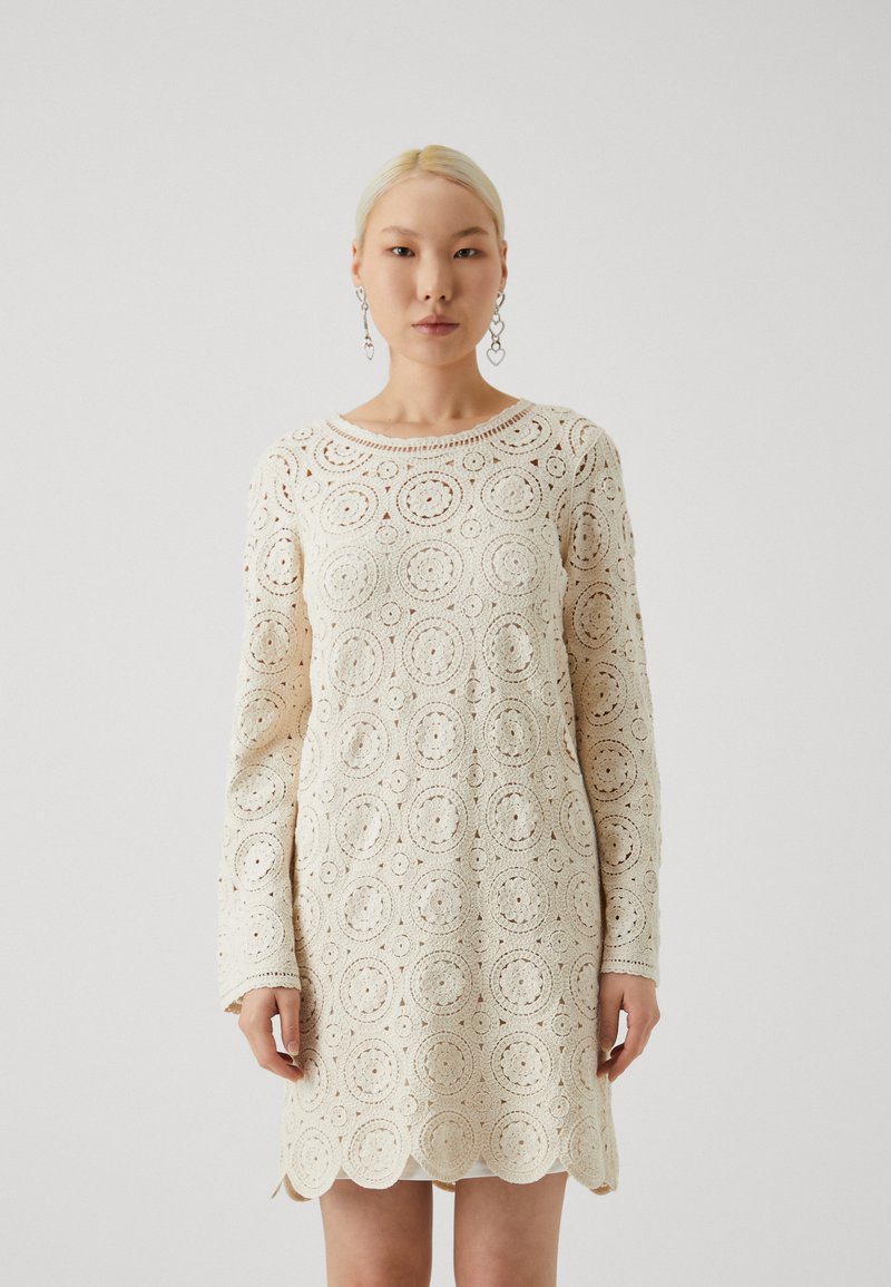Robe au crochet en crème avec des motifs circulaires, des manches longues et un ourlet festonné. Matière tricotée légère et texturée.