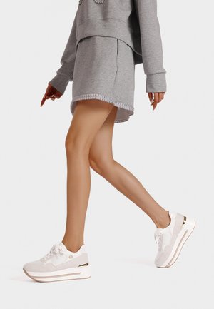 Sneakers bianchi e grigi chiari con una finitura testurizzata, lacci prominenti, dettagli metallici e una suola spessa. Indossati con un outfit grigio.