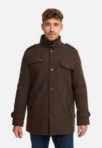 Brun frakke i uldblanding med høj krave, dobbeltradet design, store knapper og klaplommer. Har skulderstropper og en struktureret form.