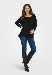 Zwarte, lange mouw trui met een ronde hals, van geweven stof, gecombineerd met blauwe skinny jeans en zwarte leren laarzen tot aan de knie.