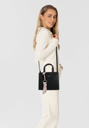 Sac à main en cuir noir avec une forme structurée, des poignées courtes et un accent en pompon rose détachable. Design simple avec un matériel minimal.