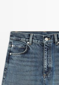 Jeans in denim con vita media, lavaggio blu, design a cinque tasche, rivetti metallici e dettagli di cucitura in evidenza.