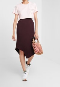 Ljusrosa kortärmad t-shirt med text, kombinerad med en mörkbordeaux midikjol med asymmetrisk fåll och en vävd väska. Vita sneakers bärs.