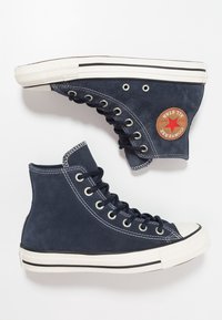 Námořnické vysoké plátěné tenisky s bílými gumovými podrážkami, stříbrnými oky a červenou hvězdou na boku. Texturovaný semišový povrch a prošívané detaily.