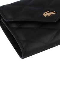 Portafoglio in pelle nera con design trapuntato, caratterizzato da un accento in oro con logo coccodrillo e cuciture visibili lungo i bordi.