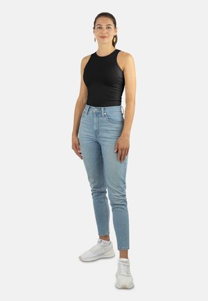 Schwarzes, ärmelloses Top, hellblaue, hochgeschnittene Jeans und weiße Sneaker. Glatte Textur, enger Schnitt und konische Beinform.