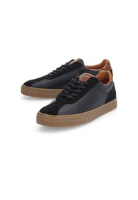 Zapatillas negras que presentan una combinación de cuero liso y ante, con detalles en marrón en el talón y la lengüeta. Suela de goma plana.
