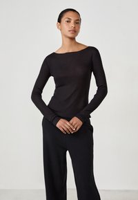 Black long-sleeve ribbed top with a wide boat neckline, fitted silhouette, and textured fabric, paired with loose black pants.