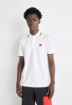Weißes Poloshirt mit einer Zwei-Knopf-Leiste, kontrastierendem schwarzen Kragen und Bündchen sowie einem kleinen roten Logopatch auf der Brust. Aus weichem Baumwollmaterial.