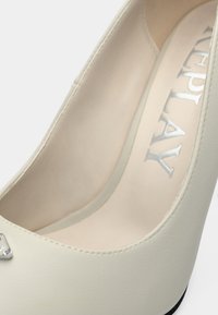 Πέργαμη λευκό γόβα με λείο εξωτερικό από συνθετικό δέρμα, στρογγυλεμένη μύτη και ασημένια λεπτομέρεια λογότυπου· με επένδυση στο πέλμα και λιτό σχεδιασμό.