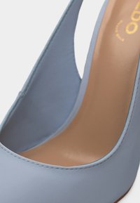 Primo piano di una scarpa con tacco alto in pelle azzurro chiaro con soletta beige e punta arrotondata.