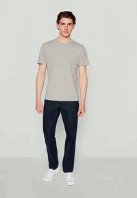 Grå bomulls-T-skjorte med rund hals, kombinert med mørkeblå jeans. Modellen har på seg hvite sneakers. Enkel, figursydd design uten mønstre.