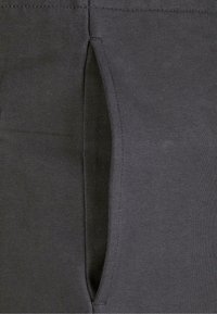 Mørkegrå leggings med slidser i siden, lavet af strækbart materiale. Teksturen er glat; sømmen er synlig langs kanterne.