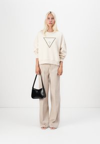 Felpa oversized color crema con un design triangolare, pantaloni beige a gamba larga e una piccola borsa nera, caratterizzata da linee eleganti e texture morbide.